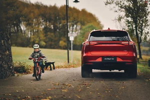 Der BYD TANG steht auf einer Straße. Links von dem Elektroauto fährt ein Kind auf dem Fahrrad lang.
